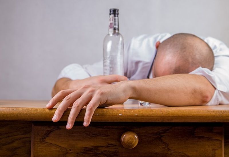 Man slumped on desk with a glass bottle