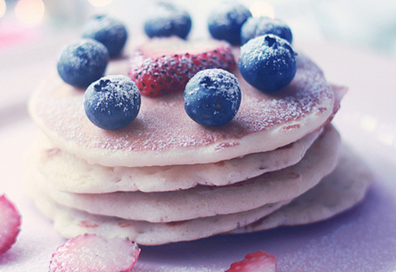 stack of pancakes with strawberries, blueberries and sugar